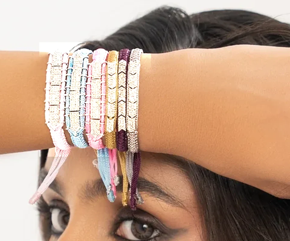 Close-up of a wrist stacked with six Caravan of Stones diamond bracelets in baby pink, sky blue, pink, gold, plum and grey